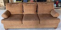 Front view of the brown corduroy upholstered sofa with visible three back cushions and three seat cushions, rolled arms, and wooden legs
