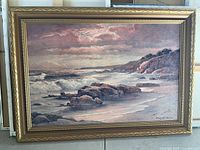 Framed print "Rocks on the Beach" by Robert Wood, showing coastal scene with rocks, beach, sea waves, and cloudy sky in warm and muted tones.