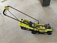 Side view of Ryobi electric lawnmower showing attached clippings bag, folded handlebar, and wheels.
