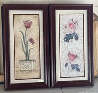 Shows two framed flower prints side by side, one with tulips in a planter and the other with pink roses. Both have dark reddish wooden frames and white mats.