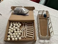 Photo showing all items included: white ceramic knobs and matching white metal handles laid in box, with screws in sealed bag, alongside Pier 1 branded rectangular wire basket with wooden base and handle.