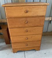 Front view of wood chest of drawers showing five drawers with wooden round knobs and smooth finish.