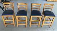 Front view of four wooden bar stools with blue cushioned seats showing overall shape and style