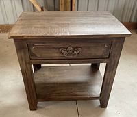 Front view of wooden side table showing drawer with intricate metal handle and bottom shelf