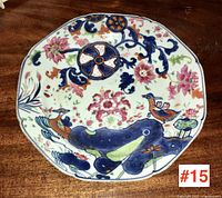 Overall front view of scalloped-edge plate showing central wheel motif, floral scrolls and bird design