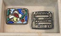 Two brooches in storage box showing enamel swirl motif brooch and openwork geometric brooch