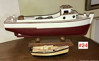 Side view of two wooden model boats, large fishing boat on stand and small rowboat in front.