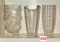 Three clear glass vases displayed from left to right: swirl-pattern art glass vase, Orrefors engraved crystal vase, pressed grid-textured vase