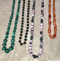 Four bead strand necklaces laid flat on a beige surface showing color and bead pattern details.