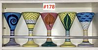 Five colorful Italian art pottery wine glasses displayed in a row showing their unique hand-painted designs and striped bases.