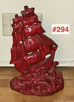 Front view of red cast iron door stop shaped like a sailing ship, showing detailed sails and wave base.