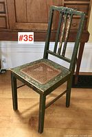 Full view of antique wooden chair showing green paint with wear and a woven cane seat in front of a wooden cabinet.
