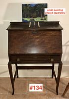 Front view of closed drop-front desk with small painting on top and lot marker