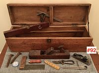 Full view of pine toolbox with antique tools laid out in front, showing various hand tools including plane, level, ruler, and nails.