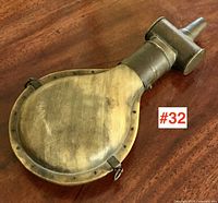 Full view of powder horn showing polished horn surface with metal rim and fitting on top with stopper.