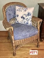 Angled front left view showing wicker armchair with seat and back cushions and decorative throw pillow
