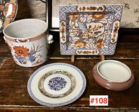 Four-piece lot arranged on wooden surface: cylindrical planter, square dish on stand, round plate, small bowl