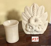 Overall view of carved alabaster relief and small alabaster cup side by side on wooden surface.