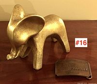Gilded elephant figure and bronze Wells Fargo belt buckle shown from the front and side angles on a wooden surface.