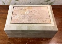Front view of Maitland Smith jewellery box with pink marble inset top and bone inlay sides on wooden table.