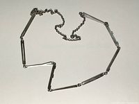 Full view of the silver modernist necklace laid out showing chain and linked bars.