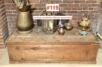 Full view of the pine wood box with several brass decorative items on top placed against a brick background.