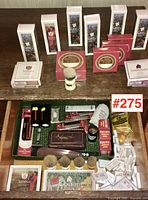 Photo overview of shaving and grooming items on wooden surface and inside drawer, showing brushes, cologne bottles, shaving sticks, comb, razor, and storage tin.