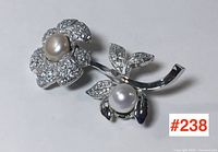 Overall view of the sterling silver flower brooch with two flower heads and pearl centers, lying on a flat surface.