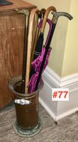 Photo of vintage canes and umbrellas arranged inside copper holder placed on floor.