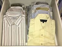 Drawer with neatly folded men's dress shirts in light colors including stripes and solid colors.