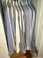 Eighteen men's dress shirts hanging in closet, displaying various striped and checked patterns in blue, white, and black.