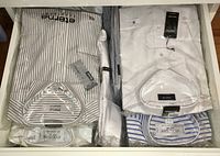 Overhead view of multiple packaged dress shirts in a drawer showing white, striped, and pinstripe designs