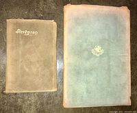 Two soft leather bound antique books laid flat showing covers, one titled 'Stevenson' and other with emblem, both with signs of edge wear and discoloration.