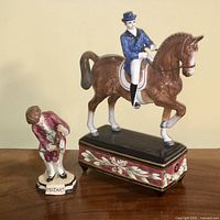 Two figurines side by side on a flat surface: Fitz & Floyd horse with rider on a decorated base, and a smaller Mozart figurine with violin labeled 'MOZART'.