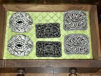 Three pairs of 1920s Art Deco shoe clips on green quilted fabric inside a wooden drawer, showing all pairs together.