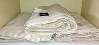 Three folded white wool blankets with satin trim stacked on shelf