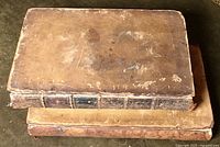 Top view of two closed antique books with worn leather covers showing heavy wear and scratches.
