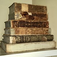 Stack of six large and medium-sized antique leather-bound books placed vertically showing spine damage, wear, and age spots.