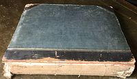 Oblique top view of atlas closed showing half-leather binding with dark blue leather spine and corners and blue marbled boards. Significant wear at edges and corners, fraying along spine.