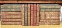 Nineteen volumes arranged in two rows showing cloth bindings in grey, green and red with gilt decoration.