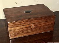 Side and front views of antique wooden dresser box showing wood grain, circular inlay on lid, and keyhole with escutcheon.
