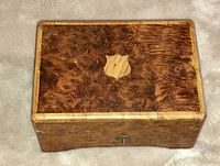 Closed view of antique rectangular wooden music box with burl veneer and keyhole on front.