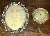 Full view of the antique oval photo frame and small desk clock on wooden surface.