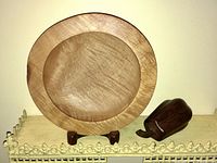 Front view of the maple bowl on stand next to the black walnut gourd on a cream-colored tray with decorative edges.