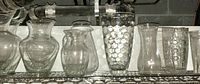 Overview of seven clear glass vases on metal shelving