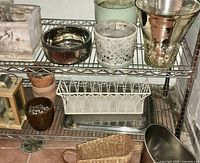 Metal shelf unit with two shelves holding assorted pottery items including planters, flower pots, containers, wicker basket, and metal bowl.