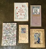 Five small antique books laid out, showing covers of varied artistic styles and titles including 'The Charm of Burne-Jones' and 'The Weed's Philosophy'.
