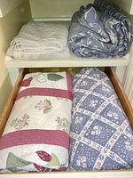 Four folded coverlets and quilts on shelf and drawer