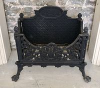 Front view of cast iron fireplace insert showing diamond lattice back panel and floral ornamental front with claw-foot legs.
