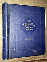 Front cover of 'The Triumph Stamp Album' showing blue leather cover with gold lettering and minor wear.